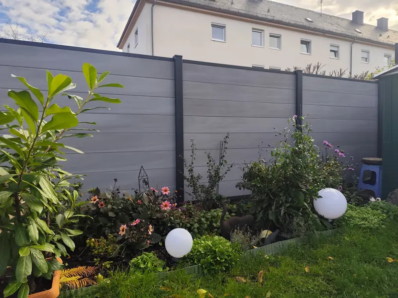 Grauer WPC-Sichtschutzzaun mit Beet und Gartenleuchten